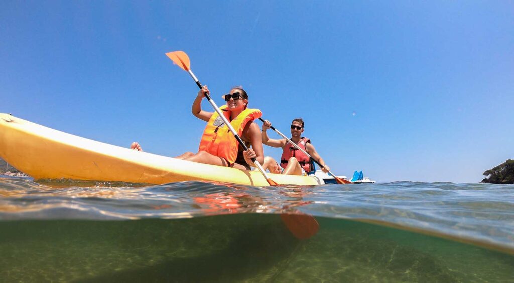 Due persone in canoa con giubbotti di salvataggio su acque limpide sotto un cielo azzurro.