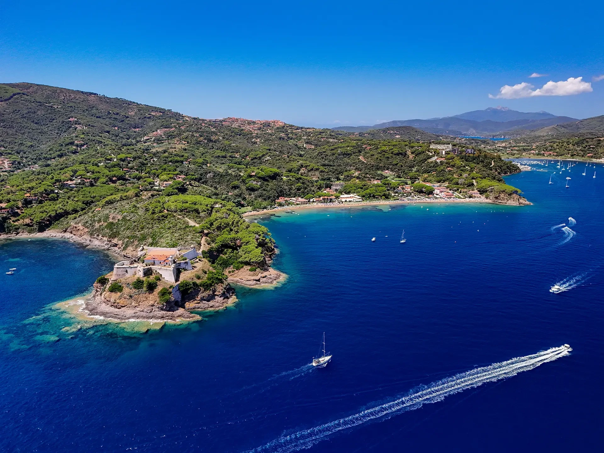 Vista aerea della costa dell'Elba con promontorio verde, mare blu intenso e barche in navigazione