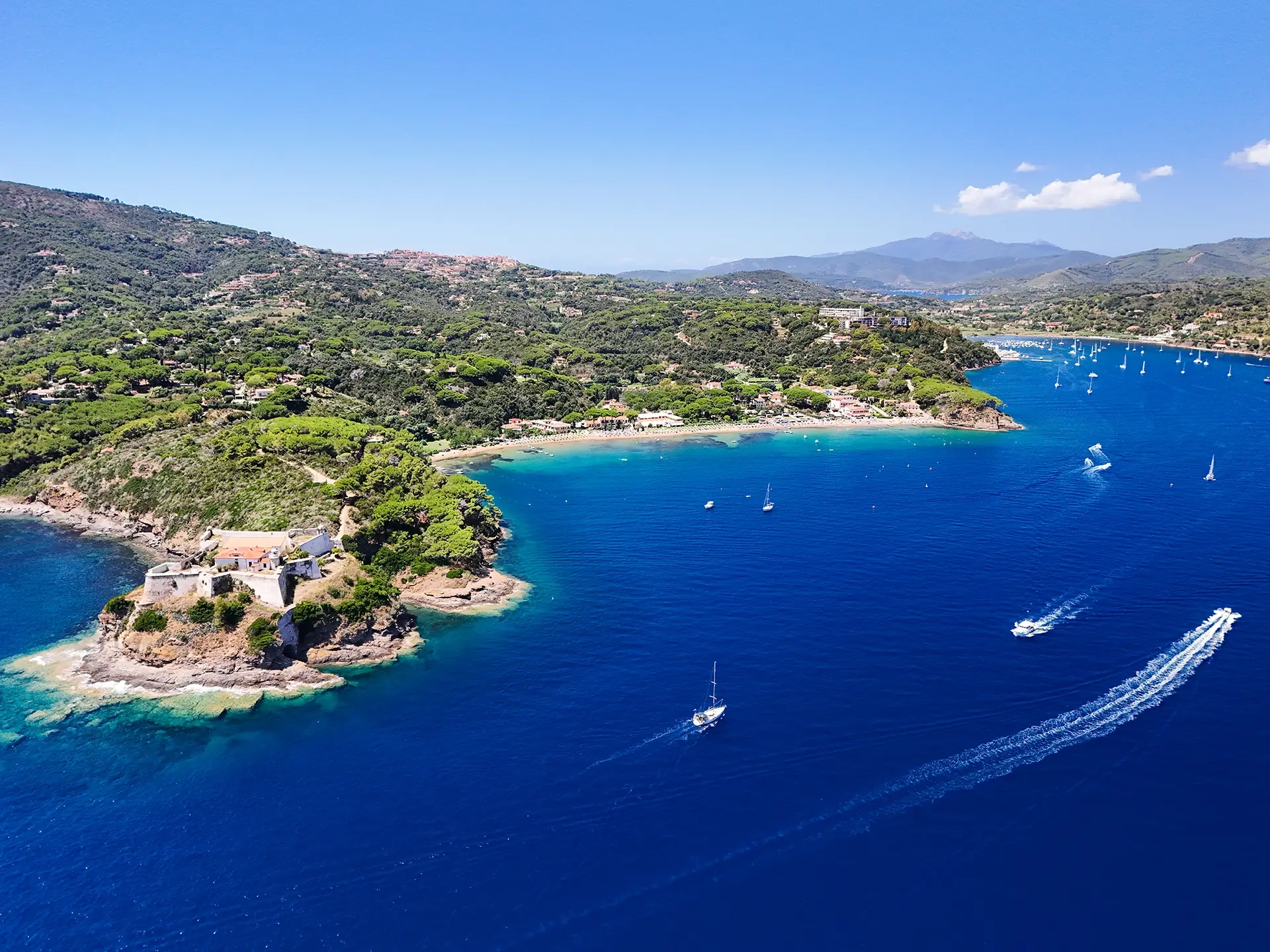 Vista aerea della baia dell'Elba con barche a vela, mare blu e collina verdeggiante