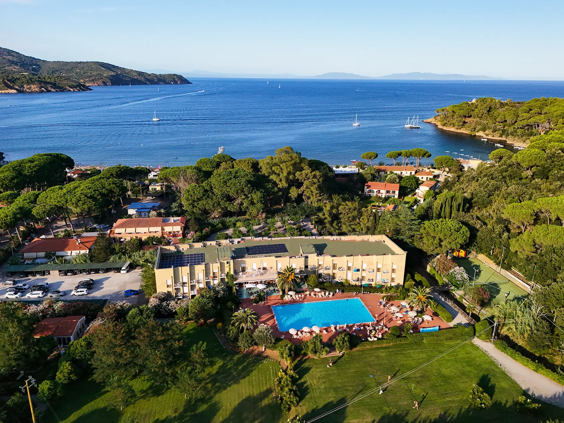 Vista aerea dell'hotel all'Isola d'Elba con piscina, pineta e baia di mare turchese sullo sfondo