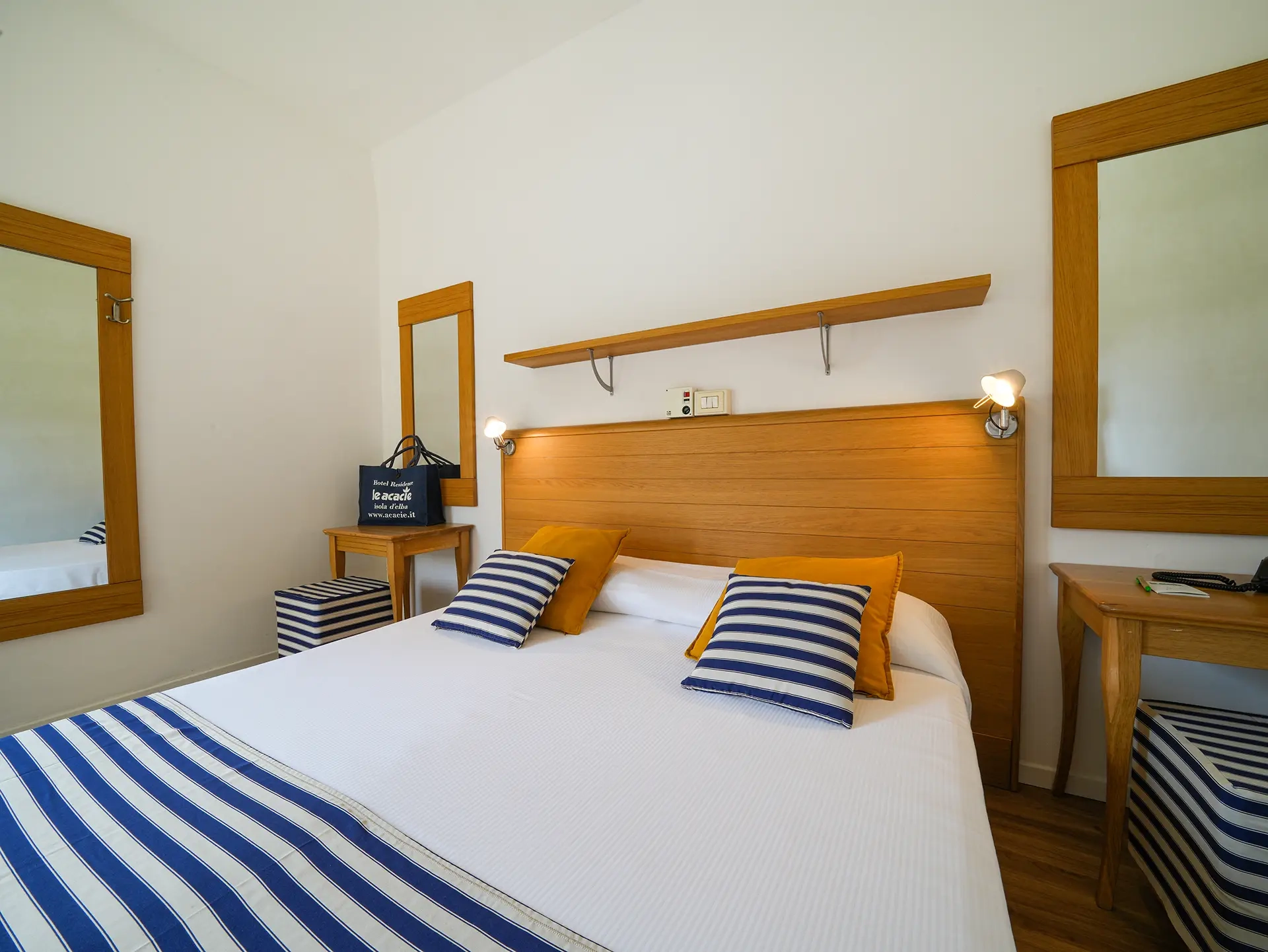 Camera con letto matrimoniale, cuscini e copriletto a righe blu e bianche, arredo in legno chiaro