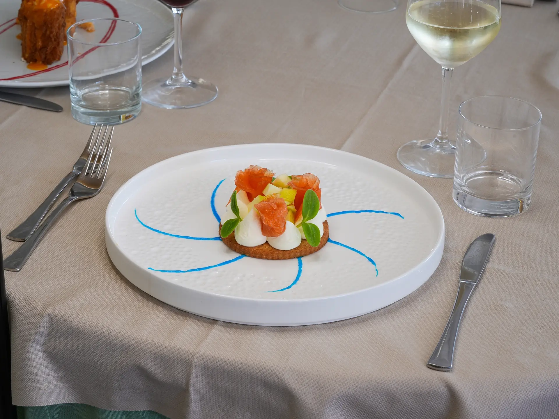 Piatto elegante con antipasto di pesce guarnito su tavola apparecchiata con calice di vino bianco