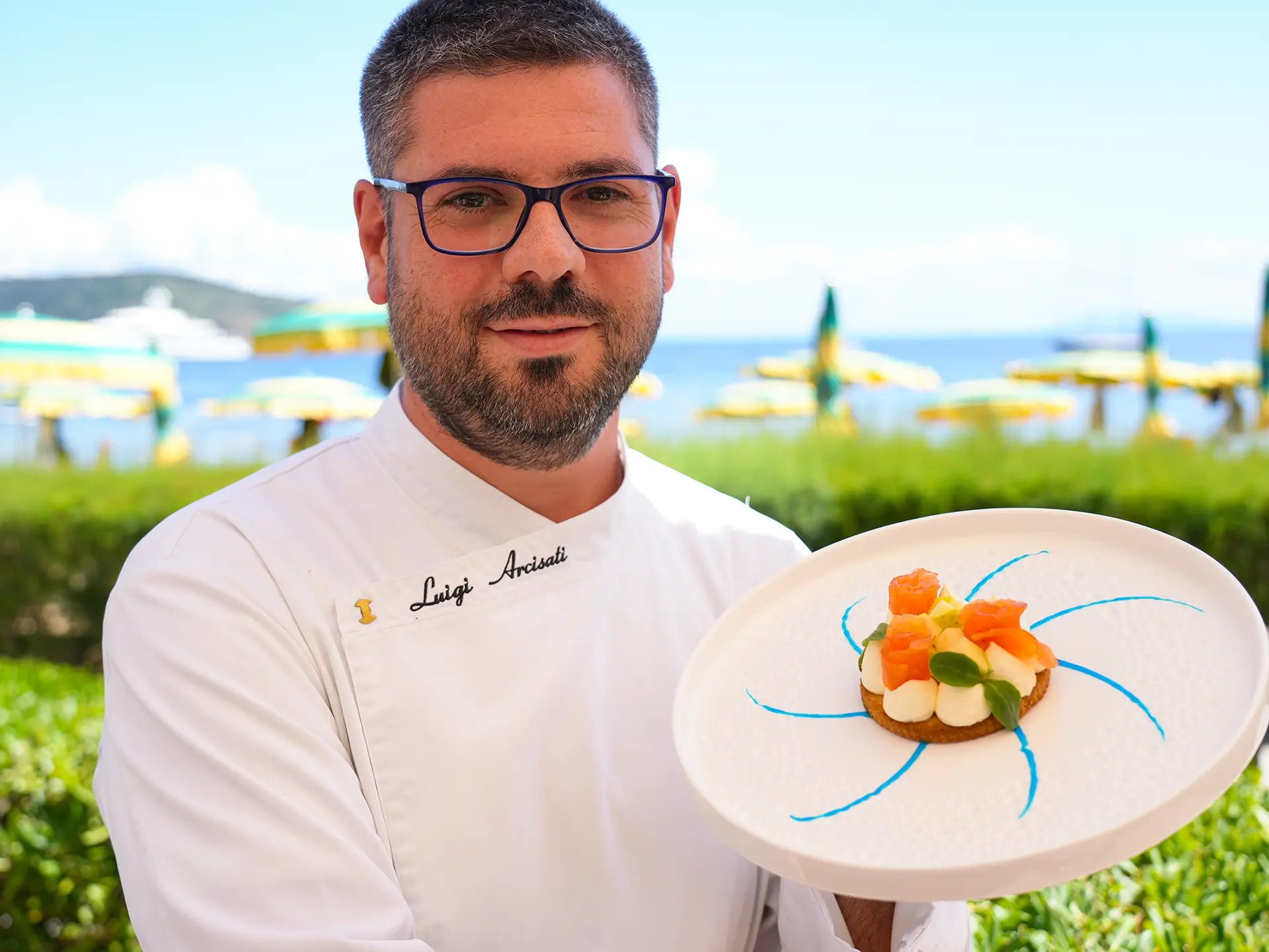 Chef mostra un piatto gourmet con crudo di pesce su terrazza vista mare all'Isola d'Elba