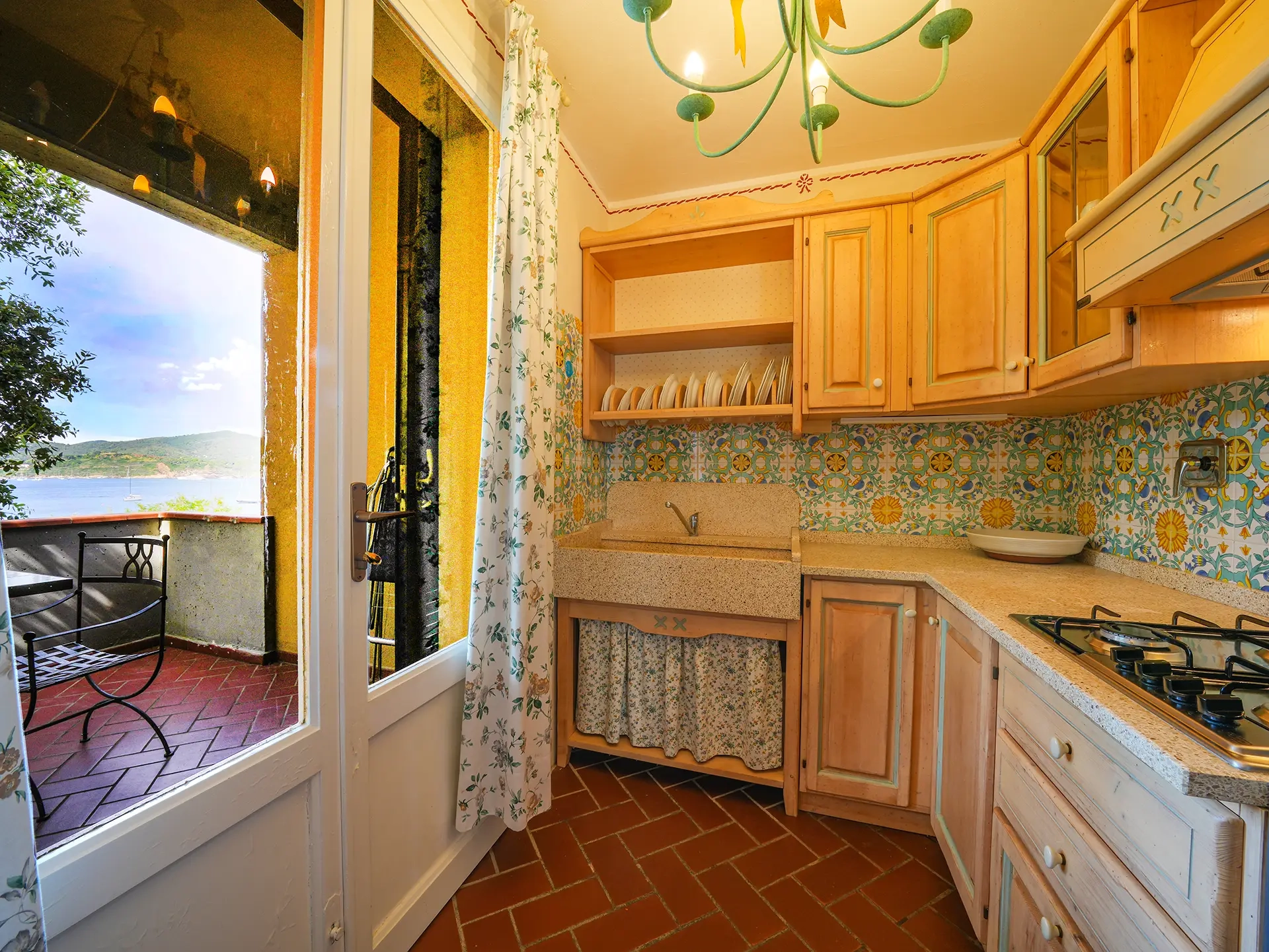 Cucina rustica con mobili in legno e piastrelle decorate, balcone con vista mare sull'Elba