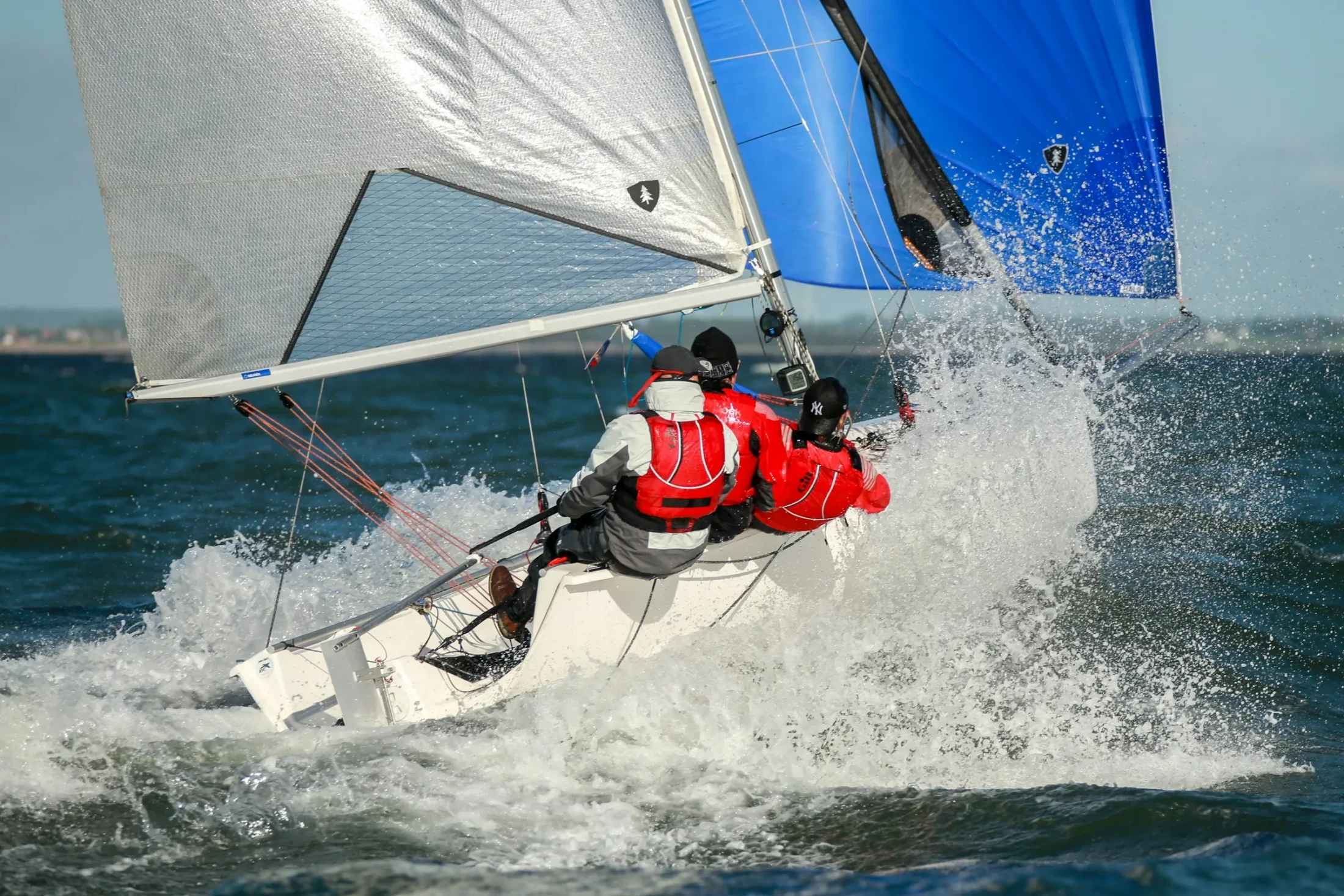 Segelboot durchpflügt spritzende Wellen vor der Elba-Küste, Crew in roter Segelkleidung in Aktion