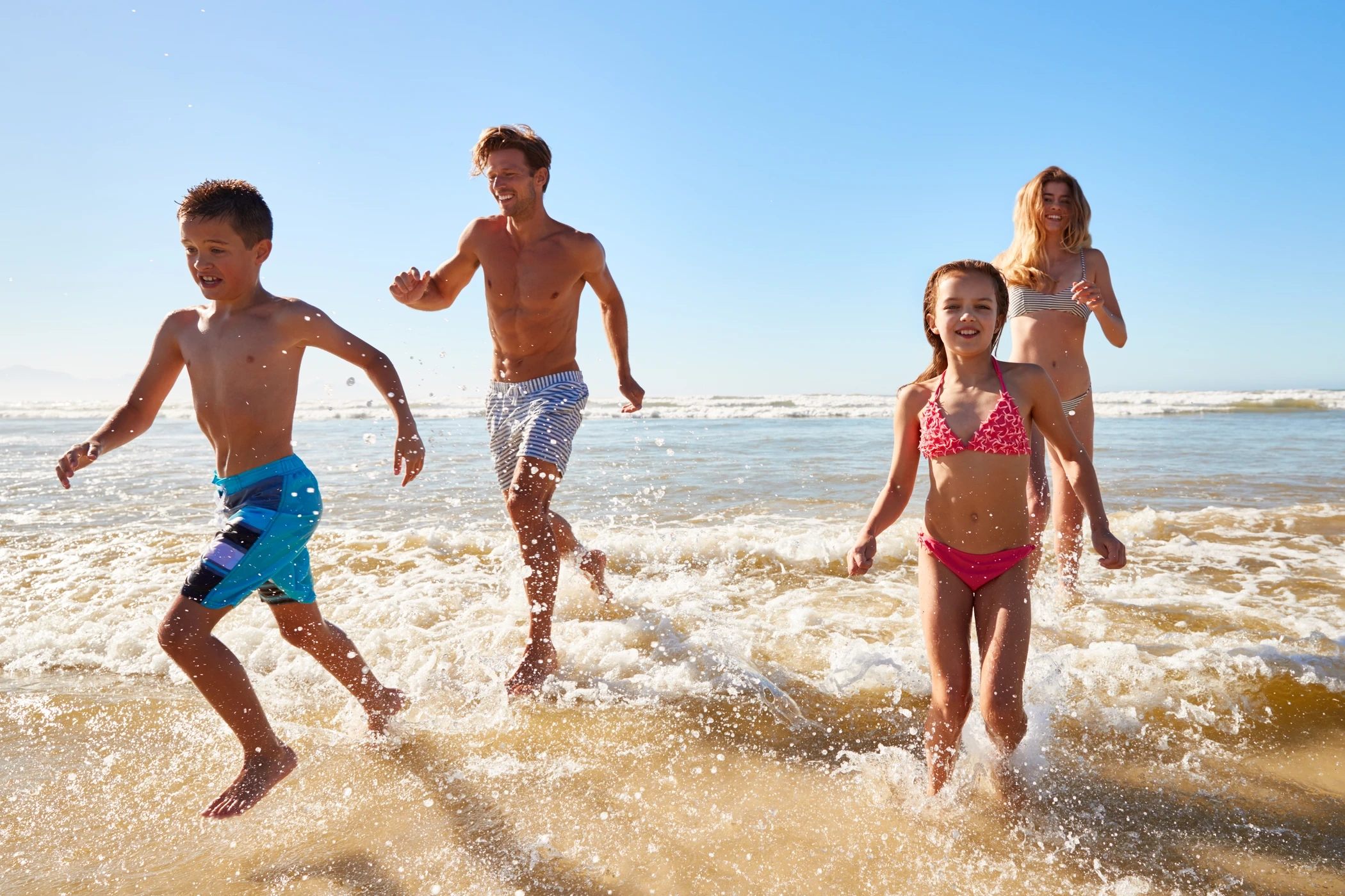 Bambini corrono ridendo tra le onde su una spiaggia soleggiata dell'Elba