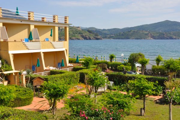 Complesso residenziale con giardino affacciato sul mare e colline sullo sfondo.